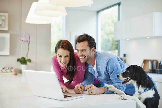 Casal usando laptop com cão na mesa — Fotografia de Stock