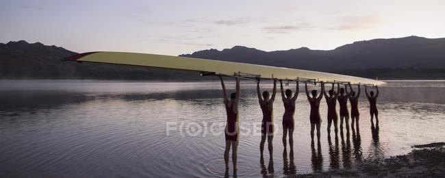 Rowing crew holding scull overhead in lake — Stock Photo