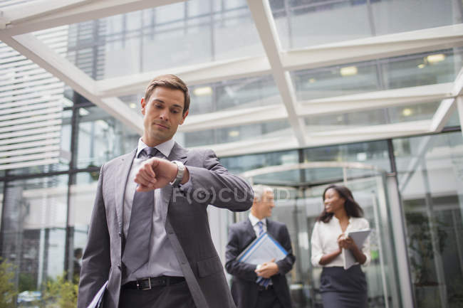 Businessman looking at watch walking out of office building — Stock Photo