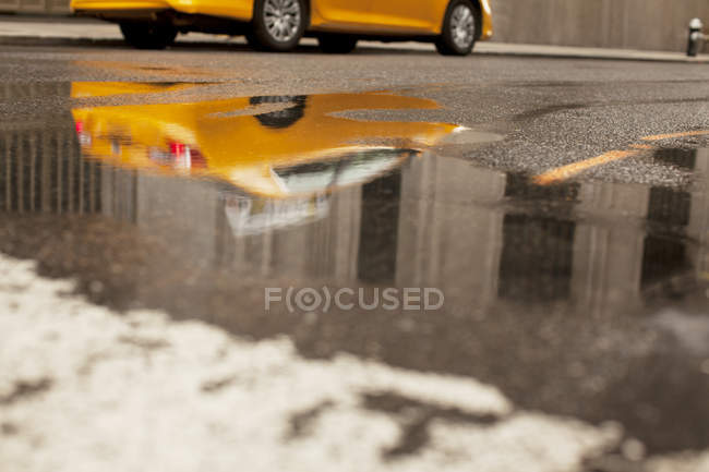 Táxi refletido na poça na rua da cidade — Fotografia de Stock