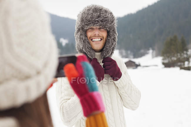 Mulher fotografando homem usando chapéu de pele no campo nevado — Fotografia de Stock