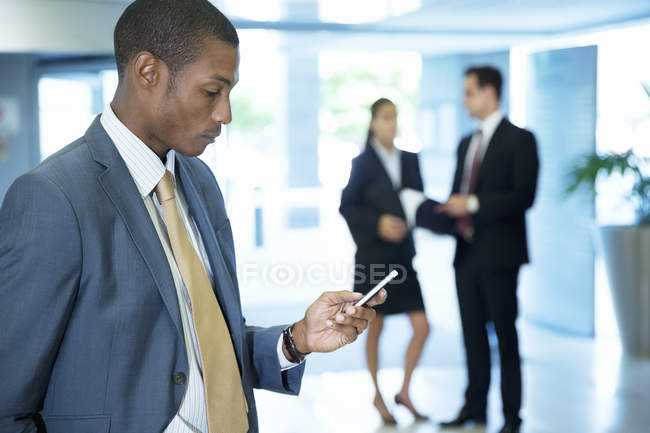 Businessman text messaging with cell phone in lobby at modern office — Stock Photo