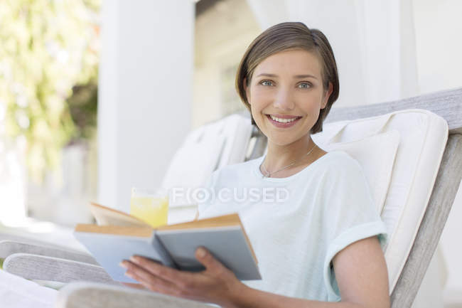 Smiling woman reading book in lawn chair — Stock Photo