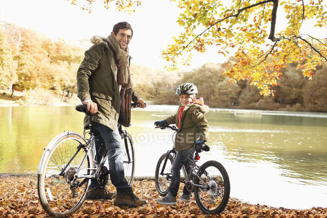 Padre e hijo sentados en bicicletas en el parque - foto de stock