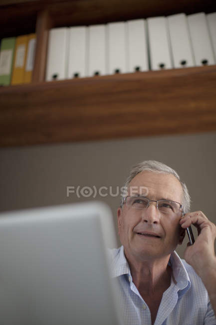 Літній чоловік розмовляє на мобільному телефоні за столом — стокове фото