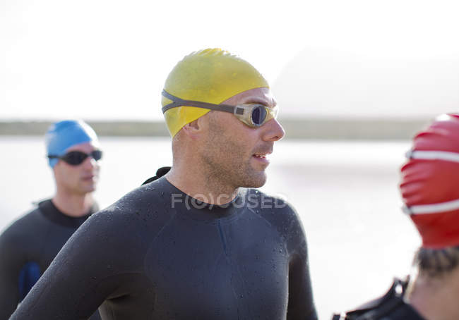 Confident and strong triathletes in wetsuits standing on beach — Stock Photo