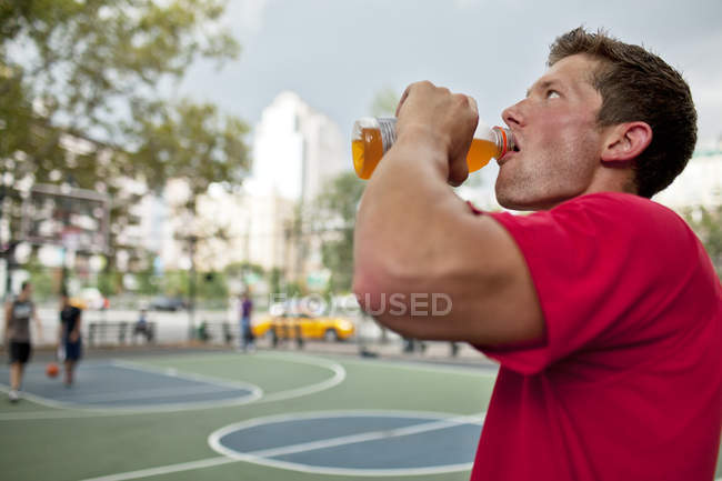 Mann trinkt Sportgetränk auf Basketballplatz — Stockfoto
