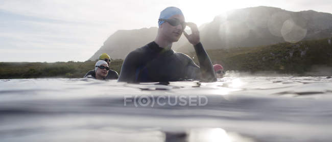 Уверенных и сильных триатлонистов в гидрокостюмах, стоящих в воде — стоковое фото