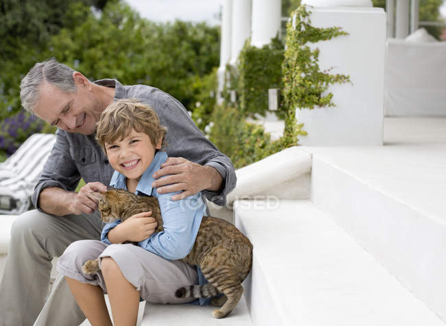 Uomo più anziano e nipote accarezzare gatto su passi — Foto stock