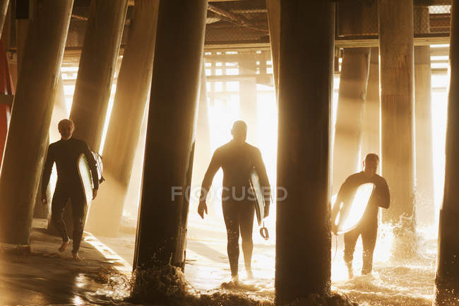 Surfistas llevando tablas debajo del muelle - foto de stock