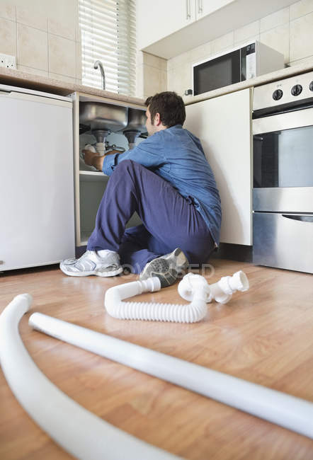 Skillful caucasian plumber working on pipes under sink — Stock Photo