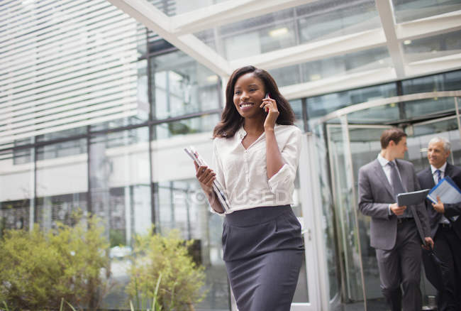 Бізнес-леді розмовляє по мобільному телефону, виходячи з офісної будівлі — стокове фото
