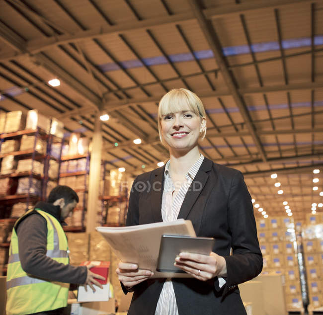Businesswoman with folder and tablet computer in warehouse — Stock Photo