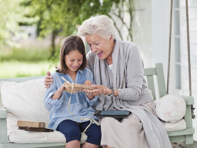 Woman giving granddaughter present in porch swing — Stock Photo