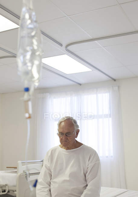 Paciente mayor sentado en la cama en la habitación del hospital - foto de stock