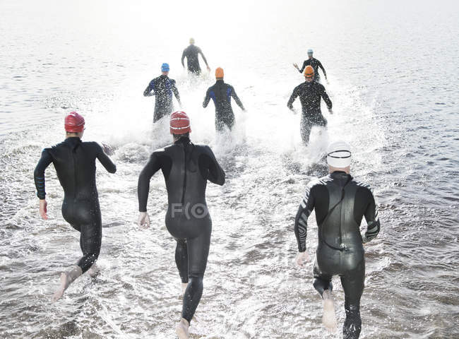 Triatleti fiduciosi e forti in mute che corrono nell'oceano — Foto stock
