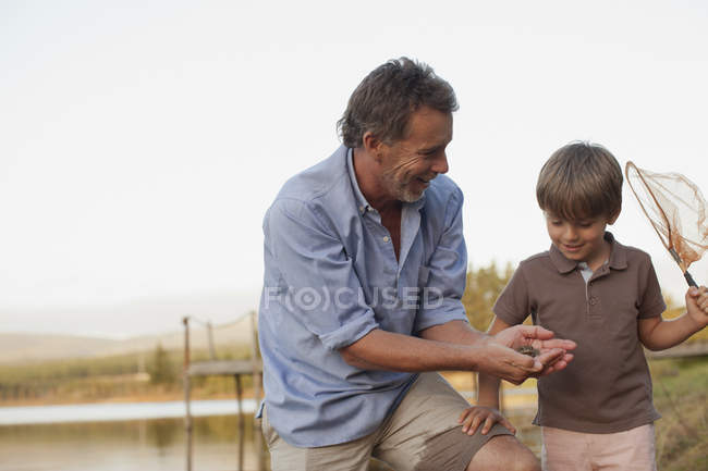 Улыбающийся дедушка и внук рыбачат на берегу озера — стоковое фото
