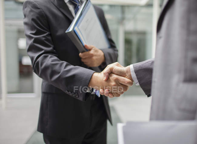 Imagen recortada de hombres de negocios estrechando la mano al aire libre cerca de la oficina moderna - foto de stock