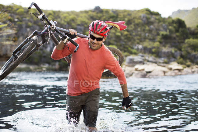 Uomo adulto caucasico che trasporta mountain bike nel fiume — Foto stock