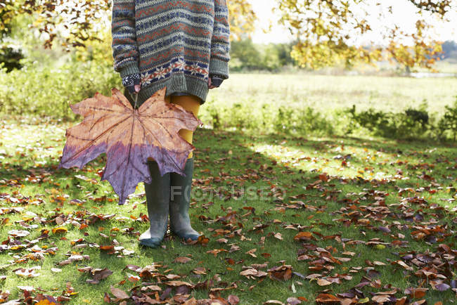 Partie basse de l'enfant tenant une grande feuille d'automne — Photo de stock