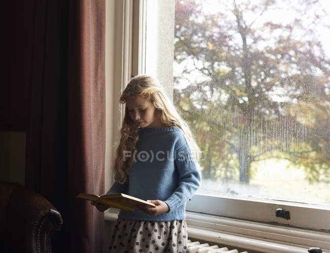 Ragazza che legge dalla finestra — Foto stock