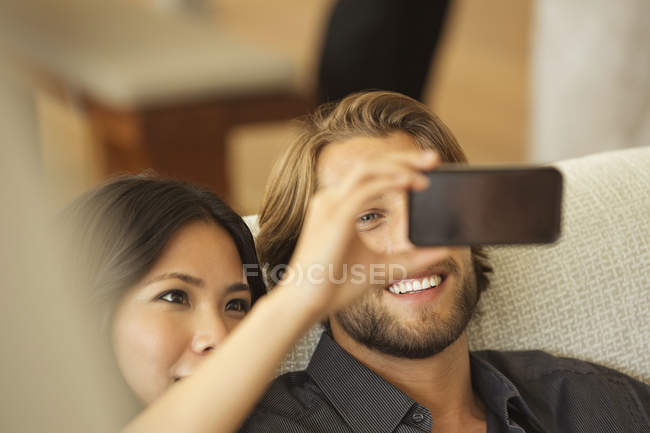 Couple utilisant le téléphone cellulaire comme caméra ensemble sur le canapé — Photo de stock