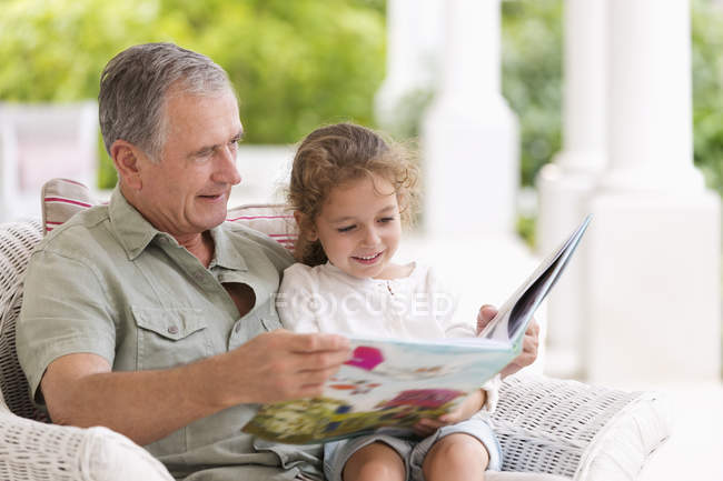 Hombre mayor leyendo a su nieta en el porche - foto de stock