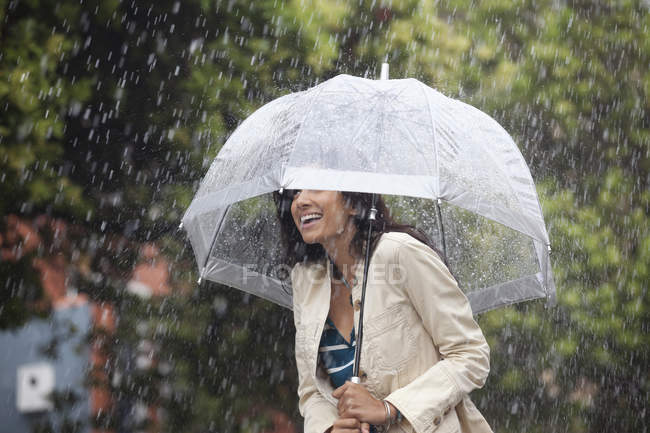 Счастливая женщина прячется под зонтиком под дождем — стоковое фото
