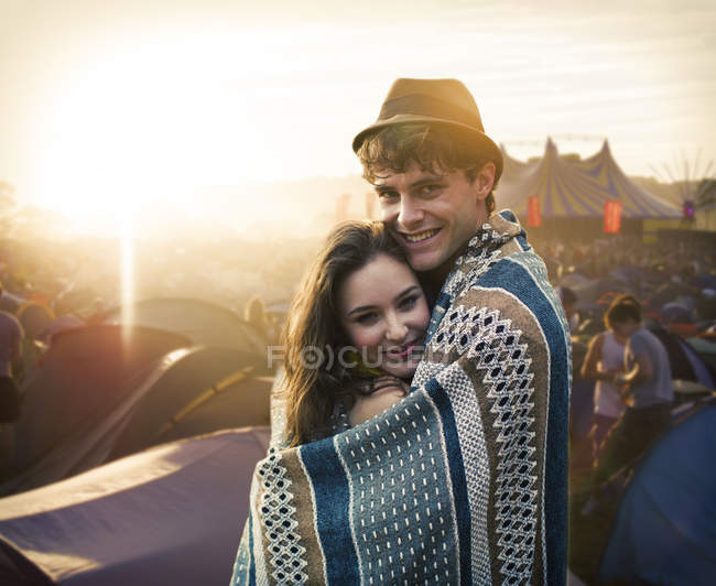 Couple wrapped in a blanket outside tents at music festival — Stock Photo