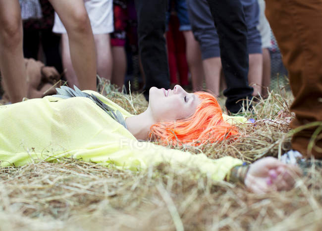 Woman in wig laying with arms outstretched in grass at music festival — Stock Photo