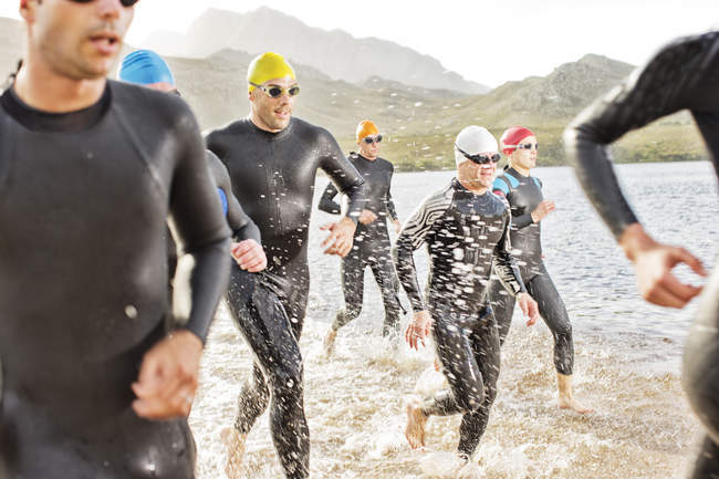 Confident and strong triathletes in wetsuits walking in waves — Stock Photo