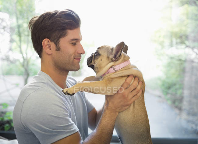 Vista lateral del hombre sonriente sosteniendo al perro en el interior - foto de stock