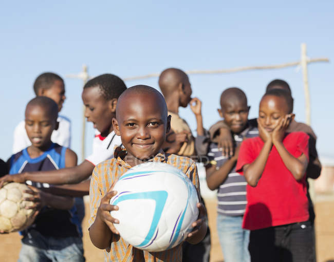 Niños africanos sosteniendo pelotas de fútbol en el campo de tierra - foto de stock