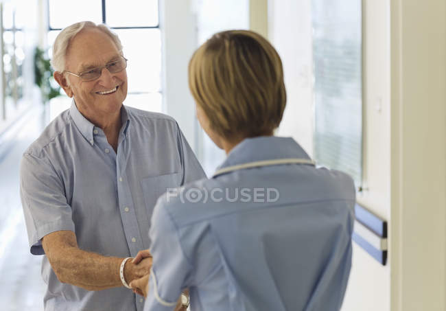 Paciente mayor y enfermera estrechando las manos en el hospital - foto de stock