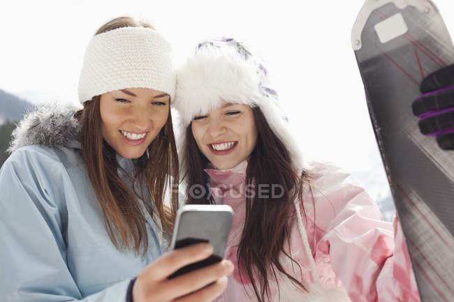 Mulheres com esquis mensagens de texto com telefone celular — Fotografia de Stock