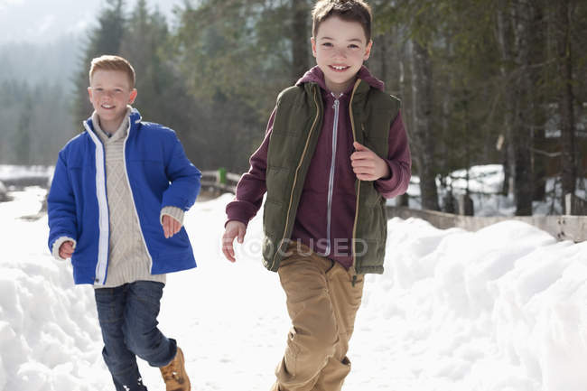Portrait of happy boys running in snowy lane — Stock Photo