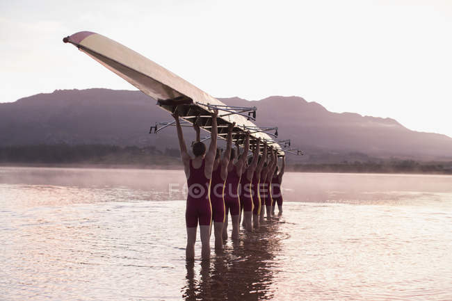 Equipo de remo que lleva barco de la fila sobre la cabeza en todavía lago - foto de stock