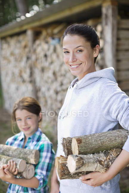 Madre e hija llevando leña al aire libre - foto de stock