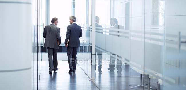 Задний вид бизнесменов, разговаривающих в современном офисном коридоре — стоковое фото