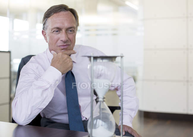 Бізнесмен дивиться пісочний годинник в сучасному офісі — стокове фото