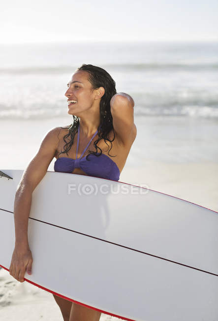 Улыбающаяся женщина держит доску для серфинга на пляже — стоковое фото
