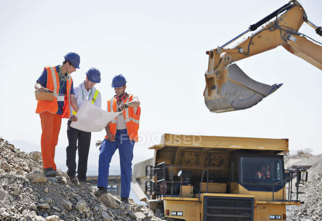 Workers and businessman reading blueprints in quarry — Stock Photo