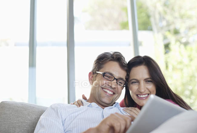 Casal usando computador tablet no sofá — Fotografia de Stock