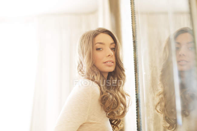 Beautiful young woman standing by mirror — Stock Photo