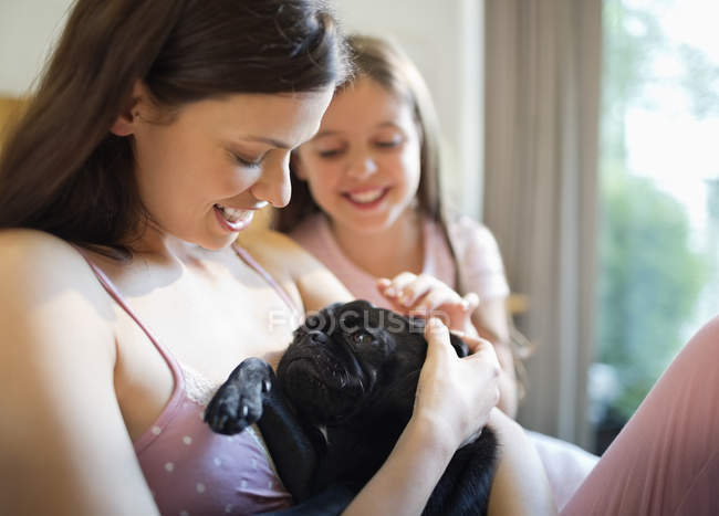 Мать и дочь ласкают собаку в постели — стоковое фото