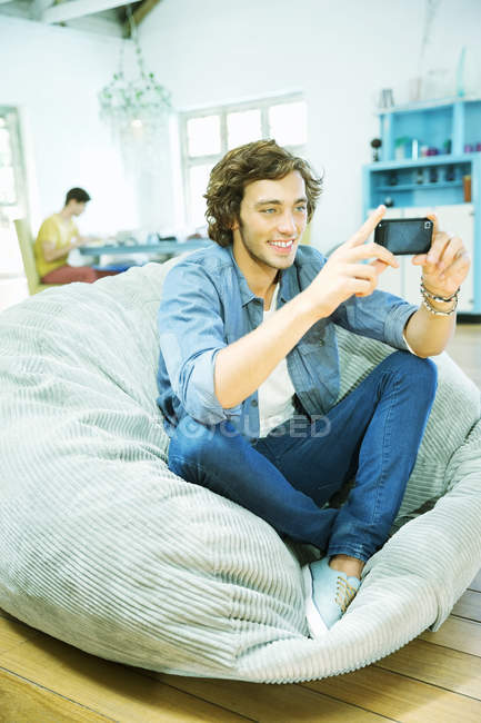 Hombre usando el teléfono celular en la silla del bolso de frijoles - foto de stock