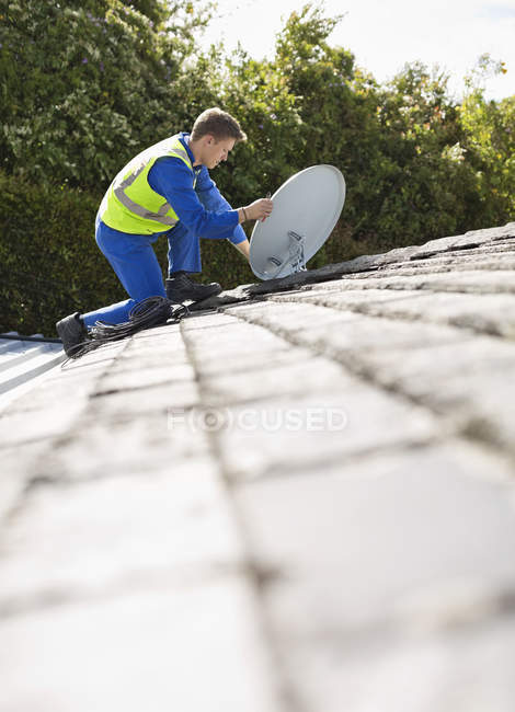 Искусный кавказский рабочий устанавливает спутниковую тарелку на крыше — стоковое фото