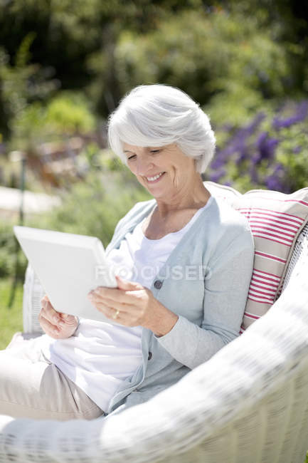 Seniorin nutzt digitales Tablet im Sessel — Stockfoto