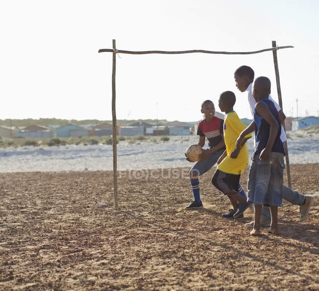 Африканские мальчики вместе играют в футбол на грязном поле — стоковое фото