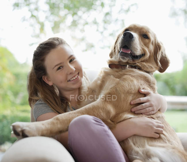 Ragazza sorridente che abbraccia cane sul divano — Foto stock